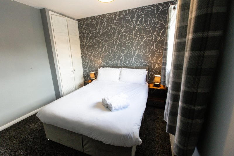 Modern bedroom with double bed, feature wallpaper, bedside tables and window with curtains