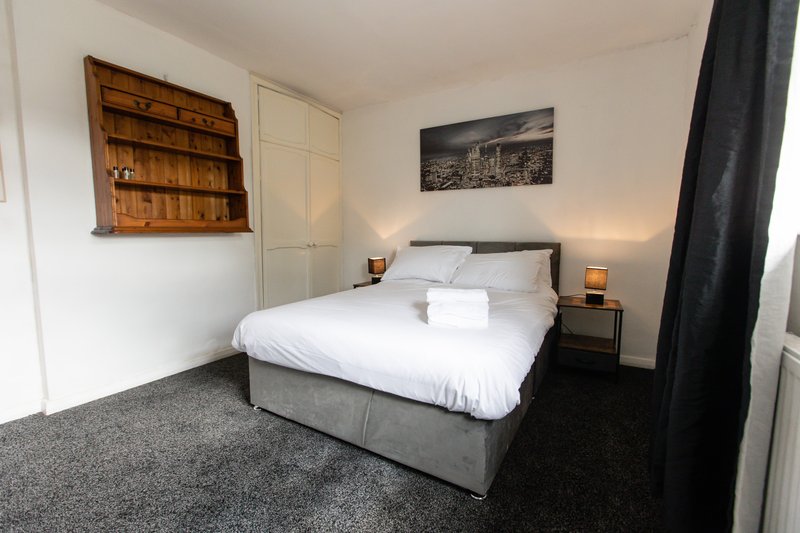 Bedroom with double bed, wooden wall shelves, cityscape artwork, and dark curtains