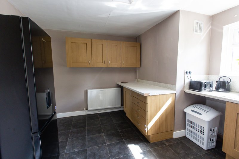 Kitchen with wooden cabinets, black refrigerator, dark tile flooring and white radiator