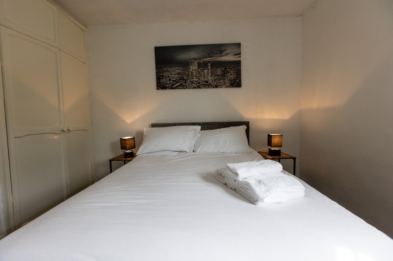 Bedroom with double bed, white bedding, black headboard, wooden nightstands with lamps, and wall art