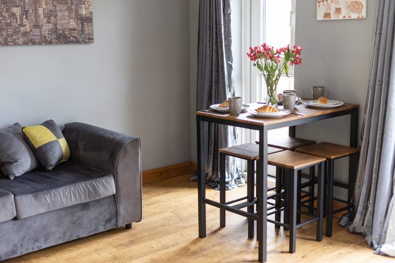 Living room with gray sofa, dining table with flowers, wooden floor and gray curtains