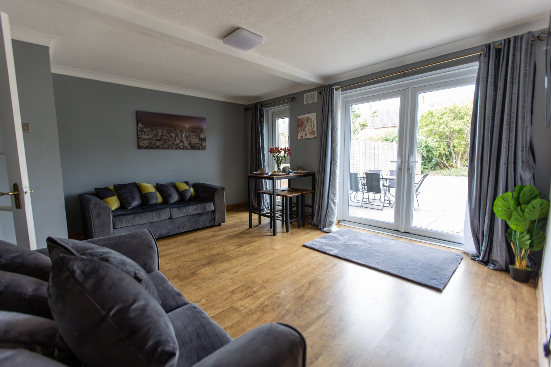 Spacious living room with grey sofas, wooden floor, and patio doors opening to garden