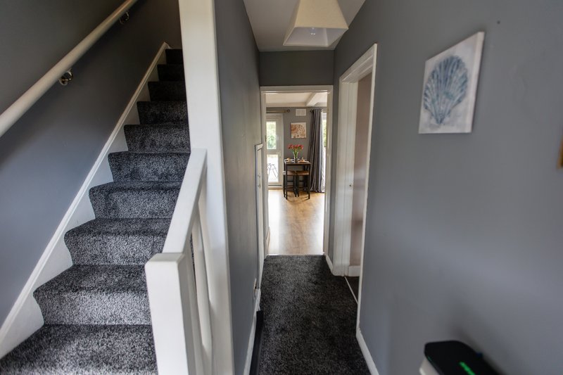 Hallway with staircase, white walls, gray carpet, and framed artwork on wall