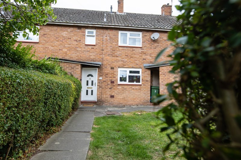 Brick semi-detached house with white door, windows, driveway and front garden with hedges