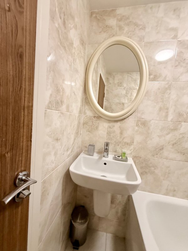 Modern bathroom with wall-mounted sink, oval mirror, and tiled walls