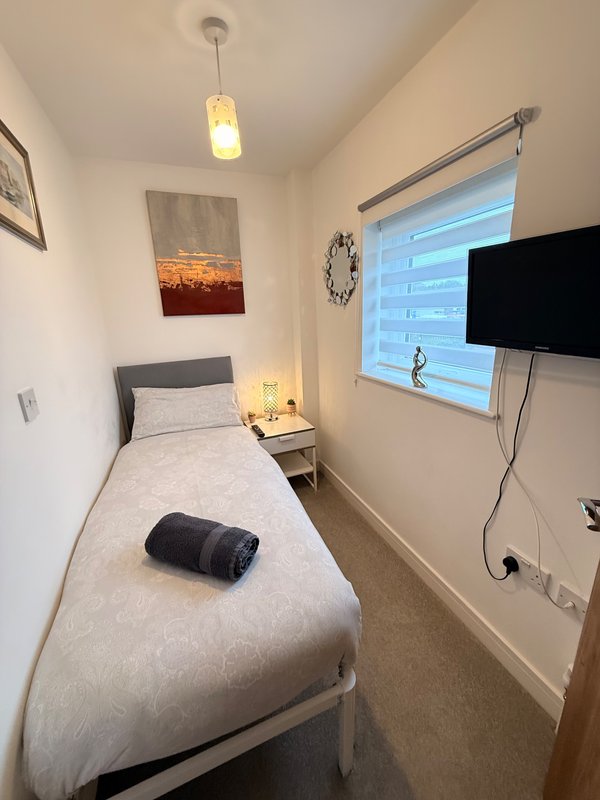 Compact bedroom with single bed, wall-mounted TV, bedside lamp and window blinds