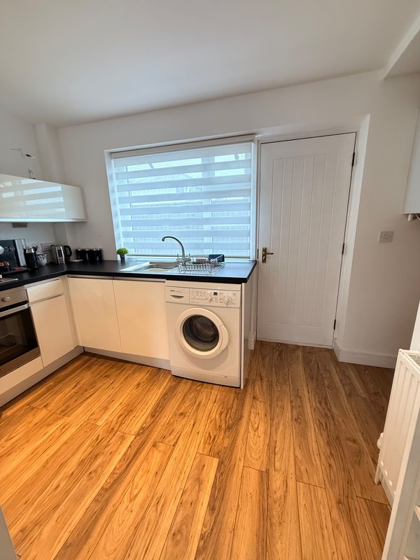 Modern kitchen with white cabinetry, integrated washing machine, wooden flooring and large window