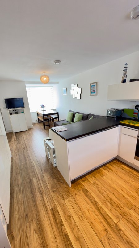 Open-plan kitchen and living area with white cabinetry, black countertop, wooden flooring and seating area