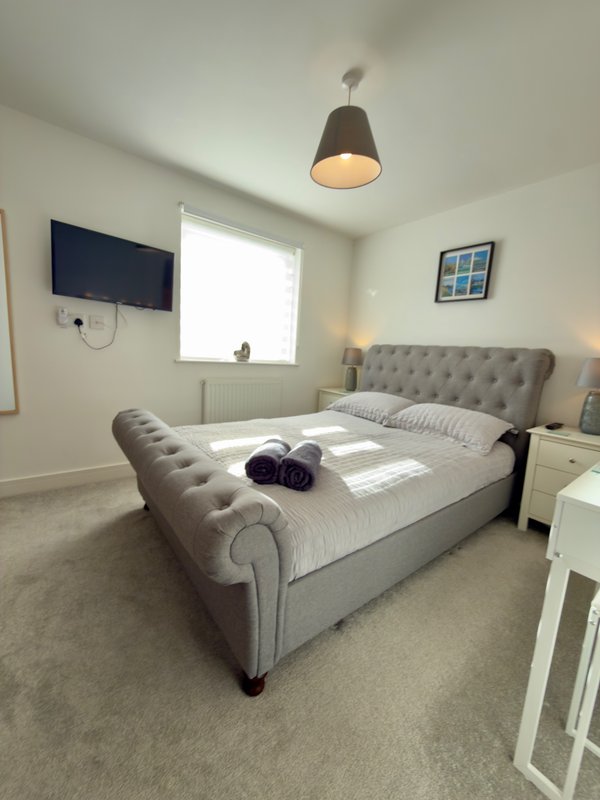 Bright bedroom with grey upholstered bed, wall-mounted TV, pendant light and window