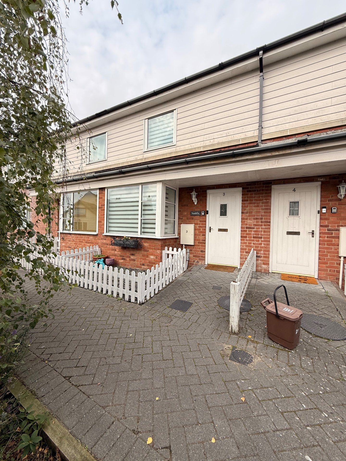 Modern terraced townhouse exterior with brick and siding, white picket fence, paved driveway and entrance doors