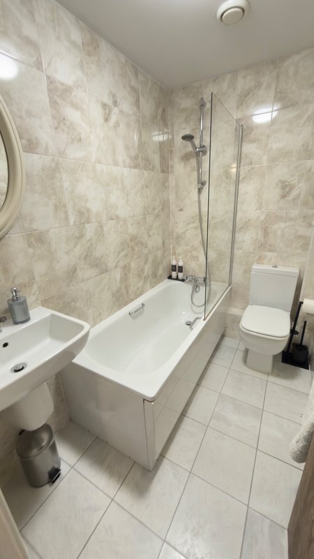 Modern bathroom with marble-effect tiles, white bath, shower enclosure, sink and toilet