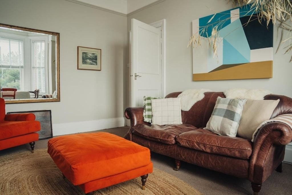 Living room with burgundy sofa, orange ottoman, patterned cushions and modern abstract wall art