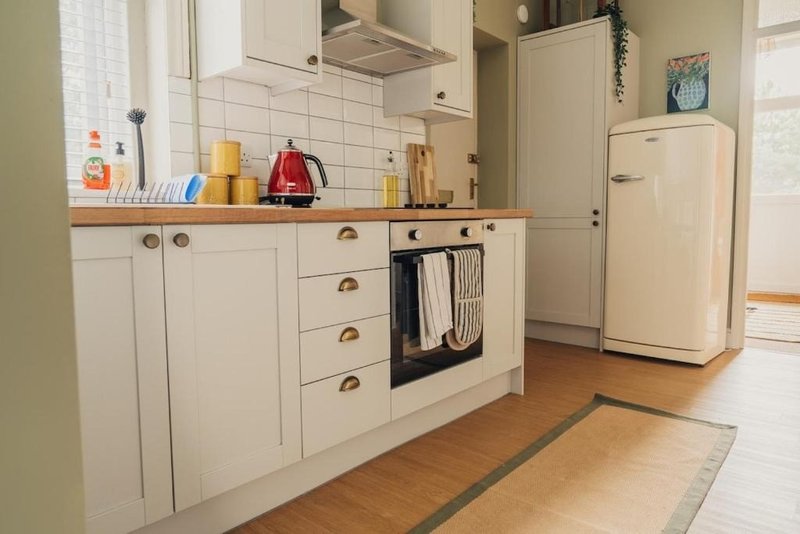 Cream kitchen with white cabinetry, wooden countertop, built-in oven and cream fridge