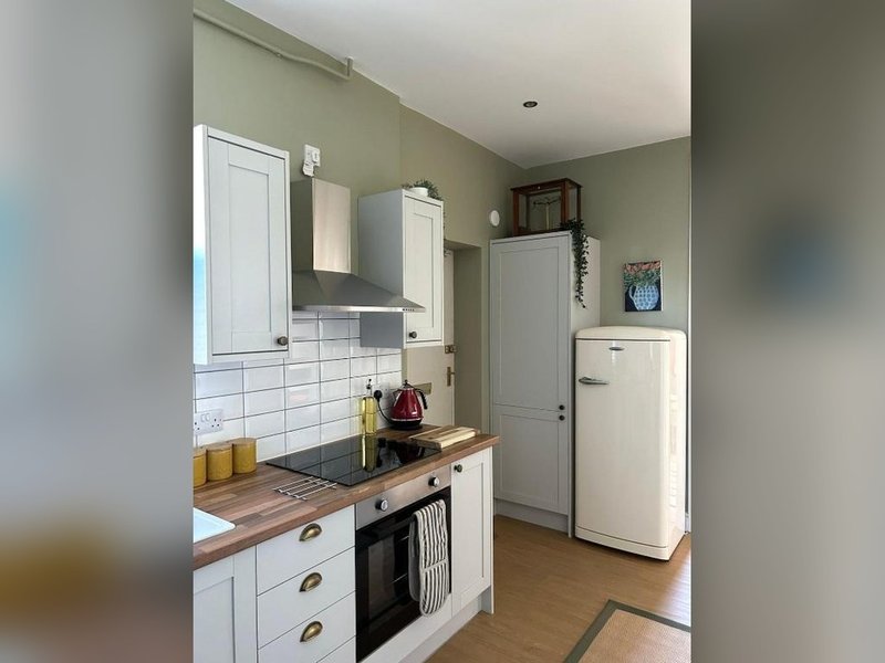Modern kitchen with white cabinetry, tile backsplash, cooktop, refrigerator and wooden countertops