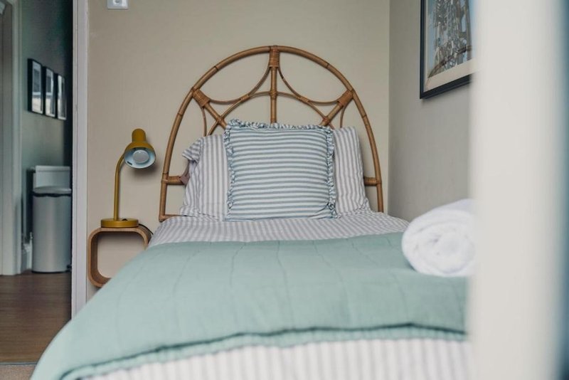 Bedroom with rattan headboard, striped pillows, light blue duvet and wooden flooring