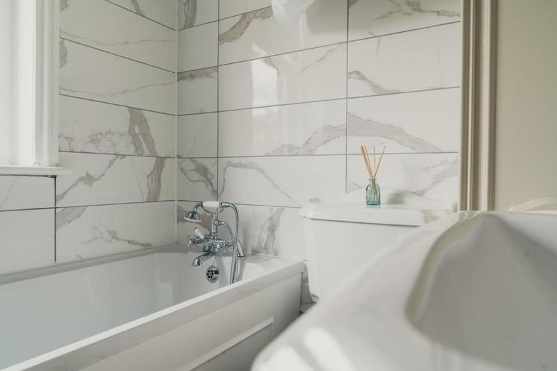 Modern bathroom with marble tile walls, bathtub, sink and decorative reed diffuser