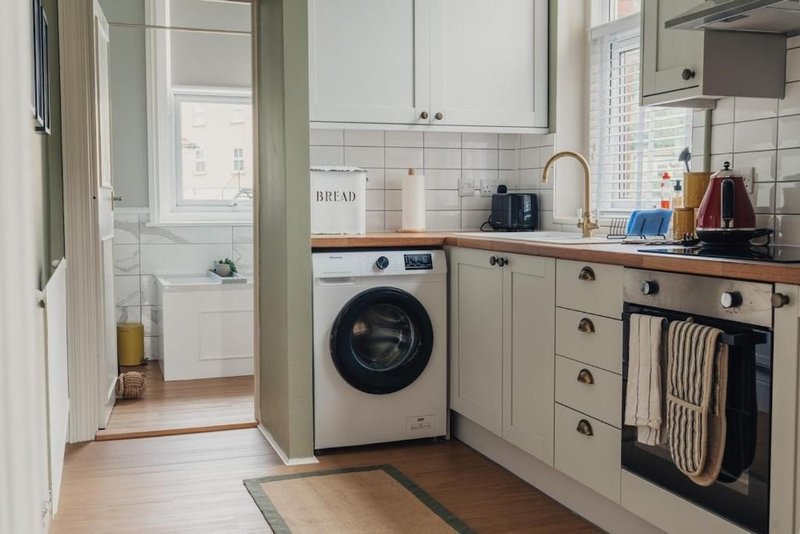 Kitchen with cream cabinets, wooden worktops, washing machine, oven and sink