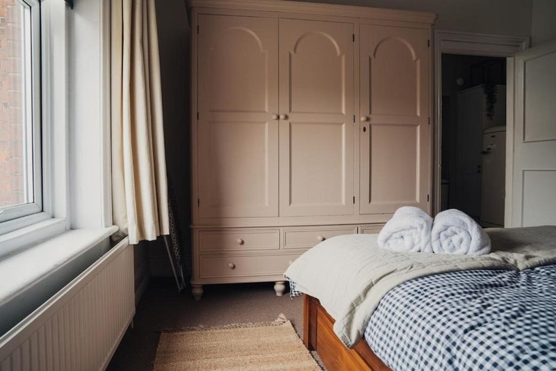 Bedroom with pink wardrobe, wooden bed, rolled towels, checkered bedding and window