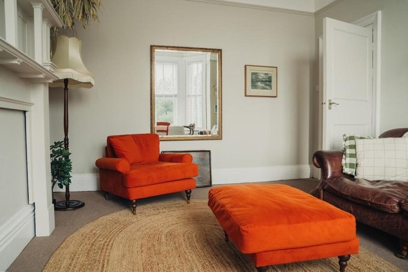 Bright living room with red armchair, orange ottoman, round jute rug and burgundy leather chair