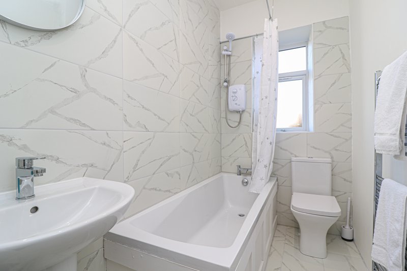 Modern bathroom with marble-effect tiling, white sink, bathtub, toilet and shower screen