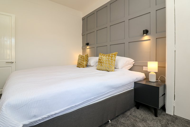 Modern bedroom with gray upholstered headboard, white bedding, yellow cushions, and bedside lamps