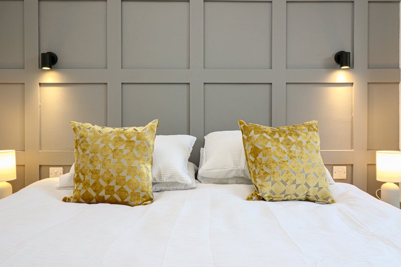 Modern bedroom with white bed, yellow patterned cushions, white pillows and wall sconces