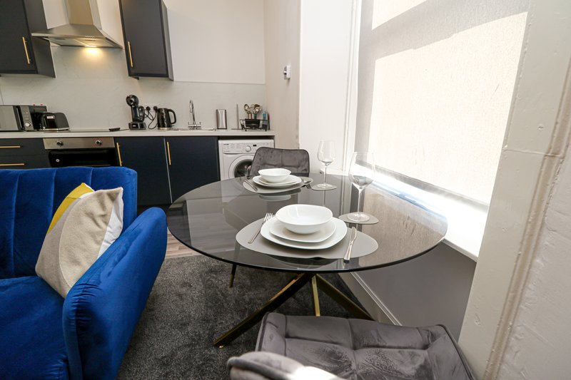 Modern open-plan kitchen and dining area with blue sofa, round glass table set for dining, and contemporary cabinetry