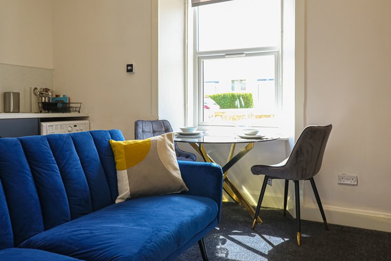 Modern living room with blue upholstered sofa, dining table, chairs and large window