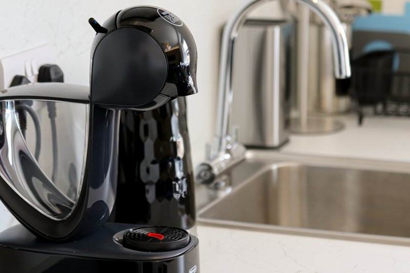 Kitchen counter with black coffee maker, glass carafe, and stainless steel sink