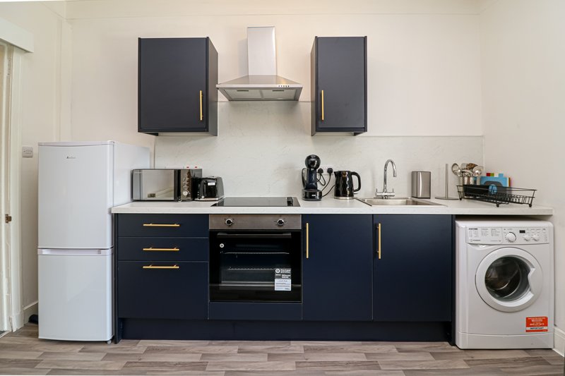 Modern kitchen with dark blue cabinetry, stainless steel appliances, white fridge and washing machine