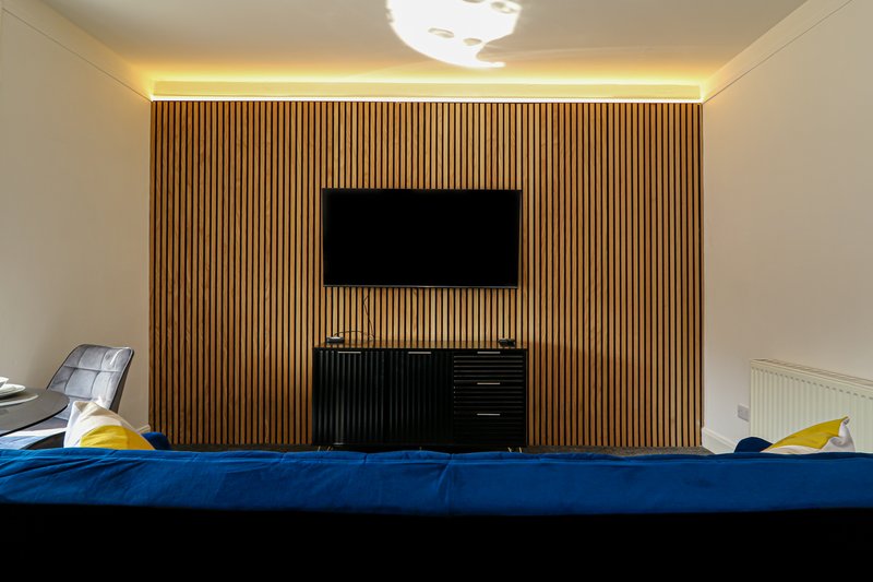 Modern bedroom with wall-mounted TV, wooden slat accent wall, and blue bedding in foreground