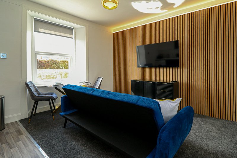 Modern living room with blue sofa, wall-mounted TV, wooden slat feature wall, and large window