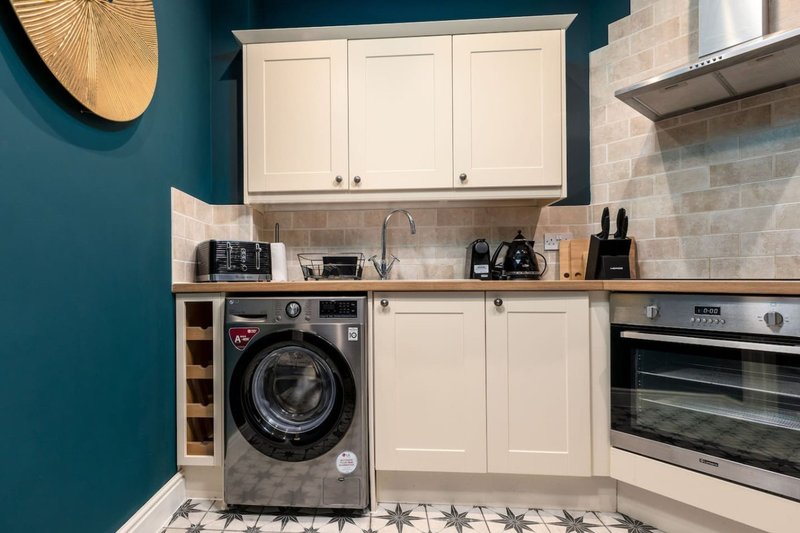 Modern kitchen with cream cabinets, washing machine, oven, and teal accent wall