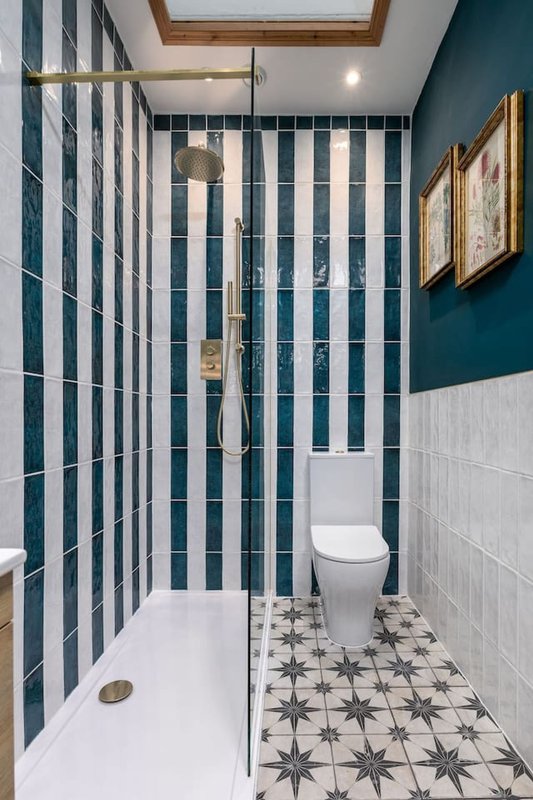 Modern bathroom with teal-striped shower enclosure, white toilet, geometric floor tiles