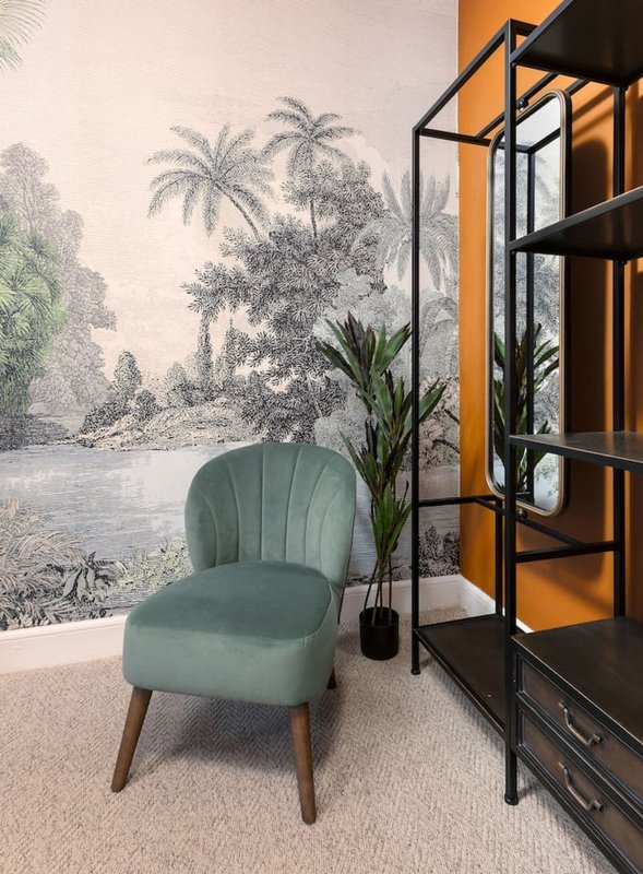 Modern bedroom with green upholstered chair, tropical mural wall art, potted plant and shelving unit