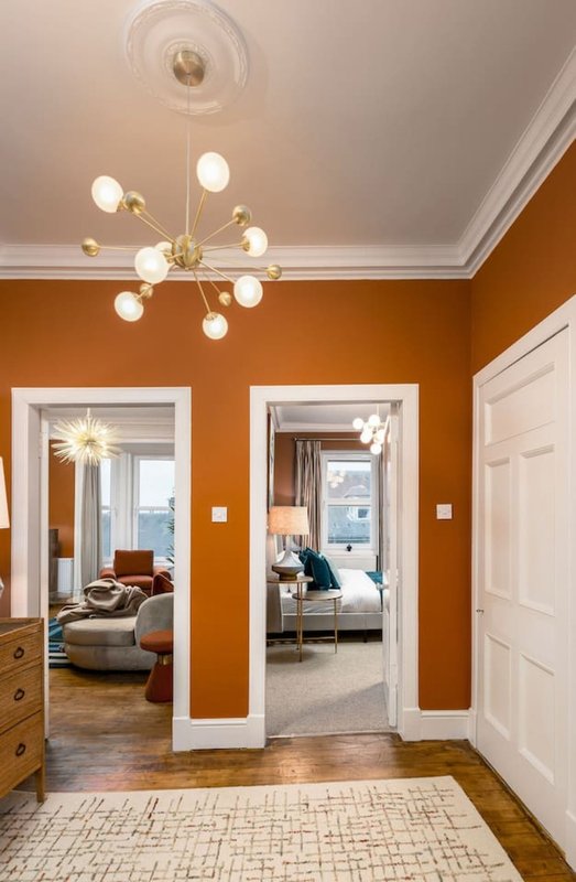 Hallway with bold orange walls, modern chandelier, white doorways and wooden floors