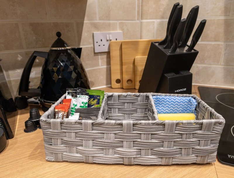 Kitchen counter with kettle, knife block, cutting boards, and storage basket containing kitchen items