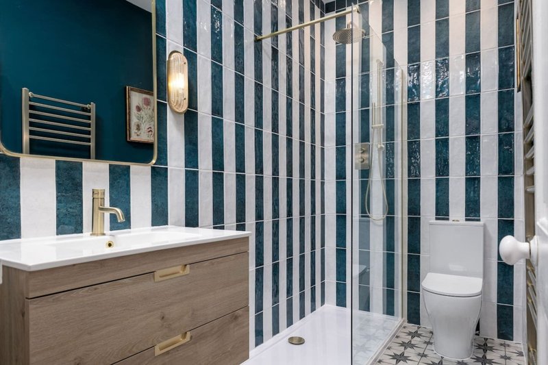 Modern bathroom with striped tile walls, wooden vanity, white sink, and glass shower enclosure