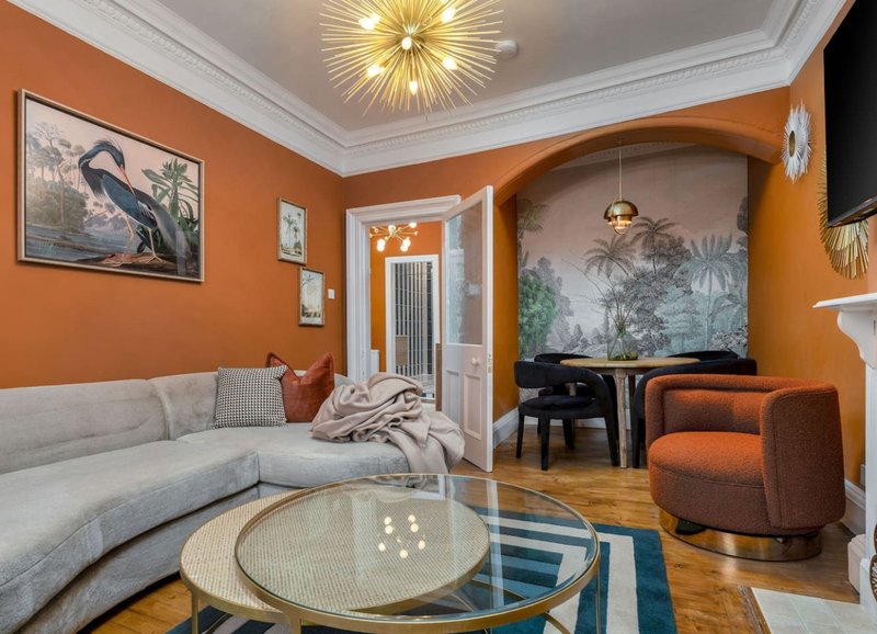 Orange and cream living room with curved sofa, glass coffee table, and modern ceiling light fixture