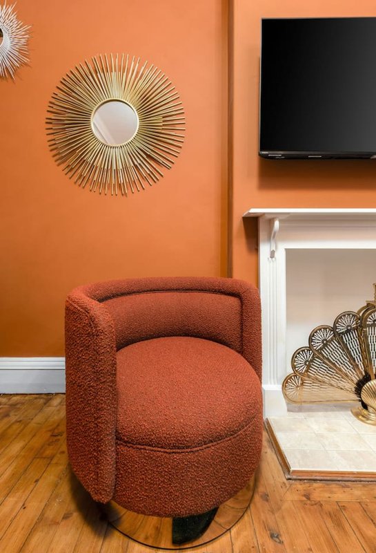 Orange living room with curved rust-colored chair, decorative mirrors, and wall-mounted TV