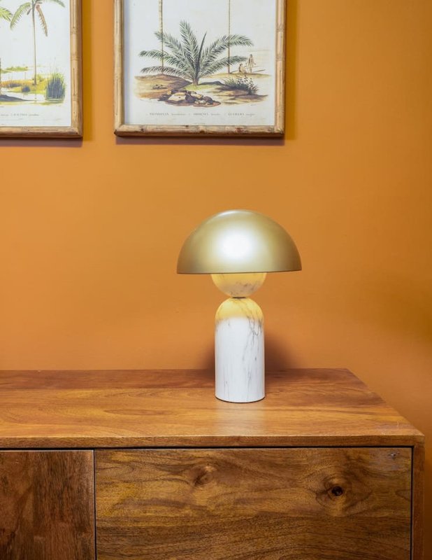 Wooden dresser with gold dome table lamp against warm orange wall, botanical artwork