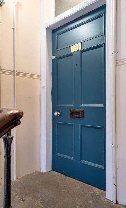 Blue front door with brass letterbox and knocker, white painted walls, concrete floor