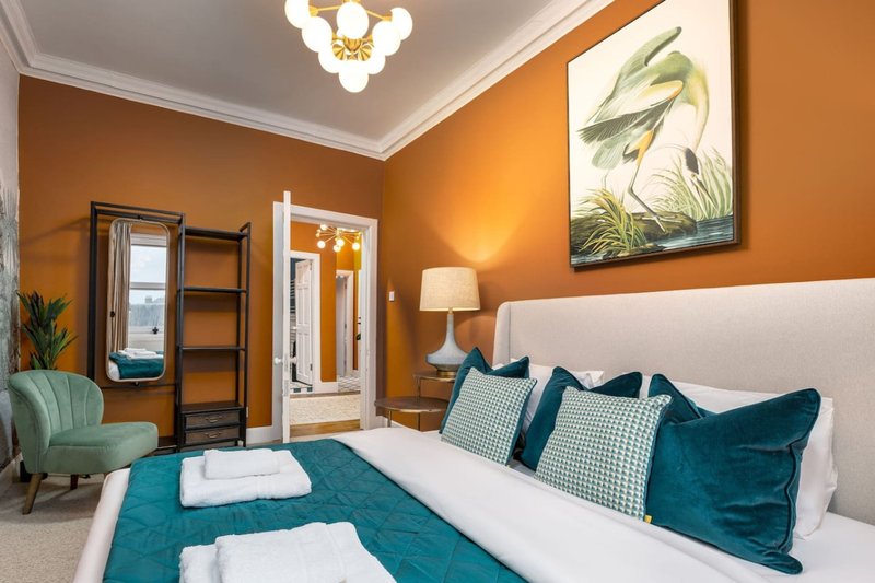 Bedroom with white headboard, teal bedding, orange walls, and modern ceiling light