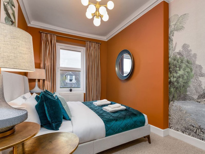 Modern bedroom with double bed, teal bedding, orange accent wall, and ceiling fixture