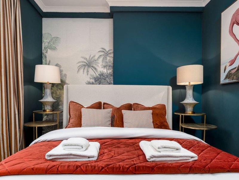 Bedroom with teal walls, white headboard, red bedding, and bedside lamps
