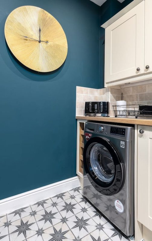 Modern laundry room with washing machine, wooden clock, teal wall and patterned floor tiles