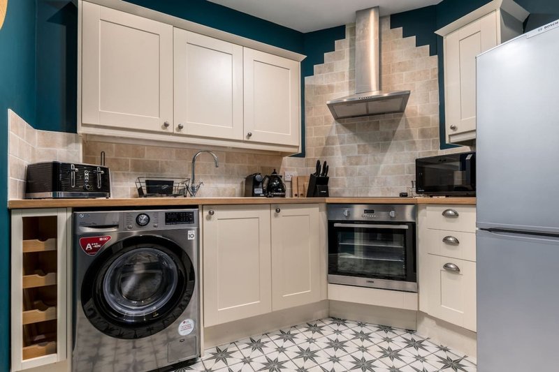 Modern kitchen with cream cabinets, stainless steel appliances, washing machine and patterned floor tiles