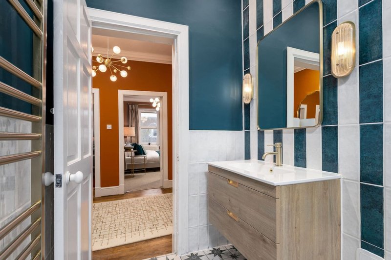 Modern bathroom with wooden vanity, tiled walls, mirror and view into bedroom beyond