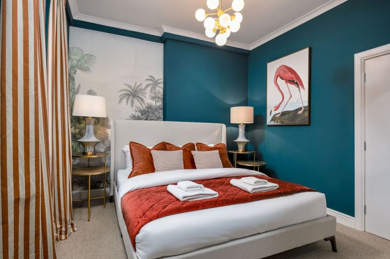 Bedroom with teal walls, white bed frame, red bedding, decorative pillows and flamingo artwork