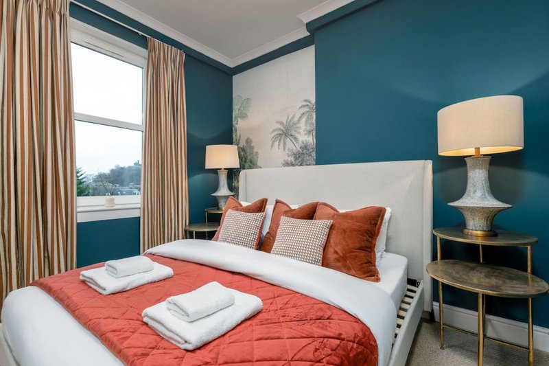 Modern bedroom with white bed, coral bedding, teal accent wall, and window with curtains